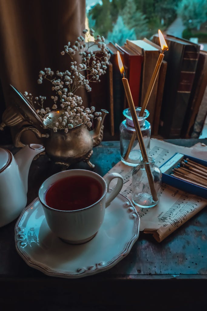 A cozy setup featuring a cup of tea, candles, and books on a vintage table by the window; an inviting space for inner exploration.