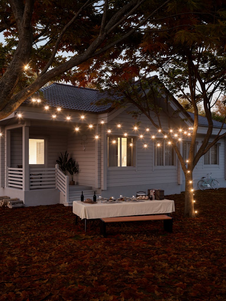 Charming evening outdoor dining setup under string lights and autumn leaves.